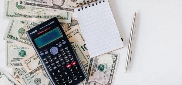 calculator and notepad placed over stack of usa dollars